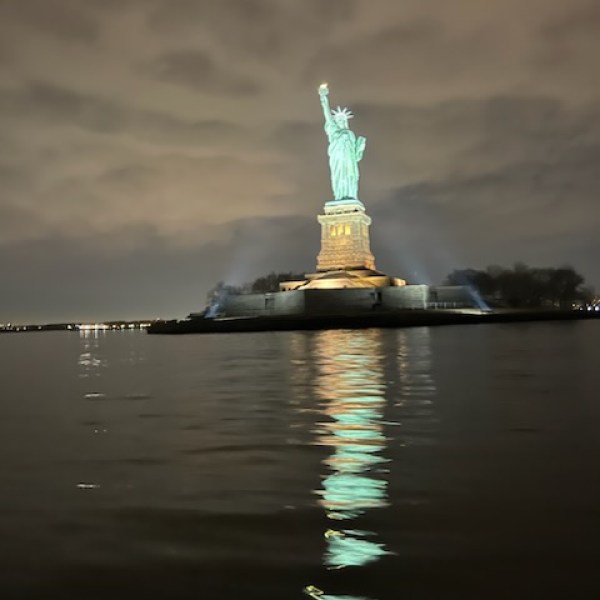 Statue of Liberty illuminated at night with reflection on water.