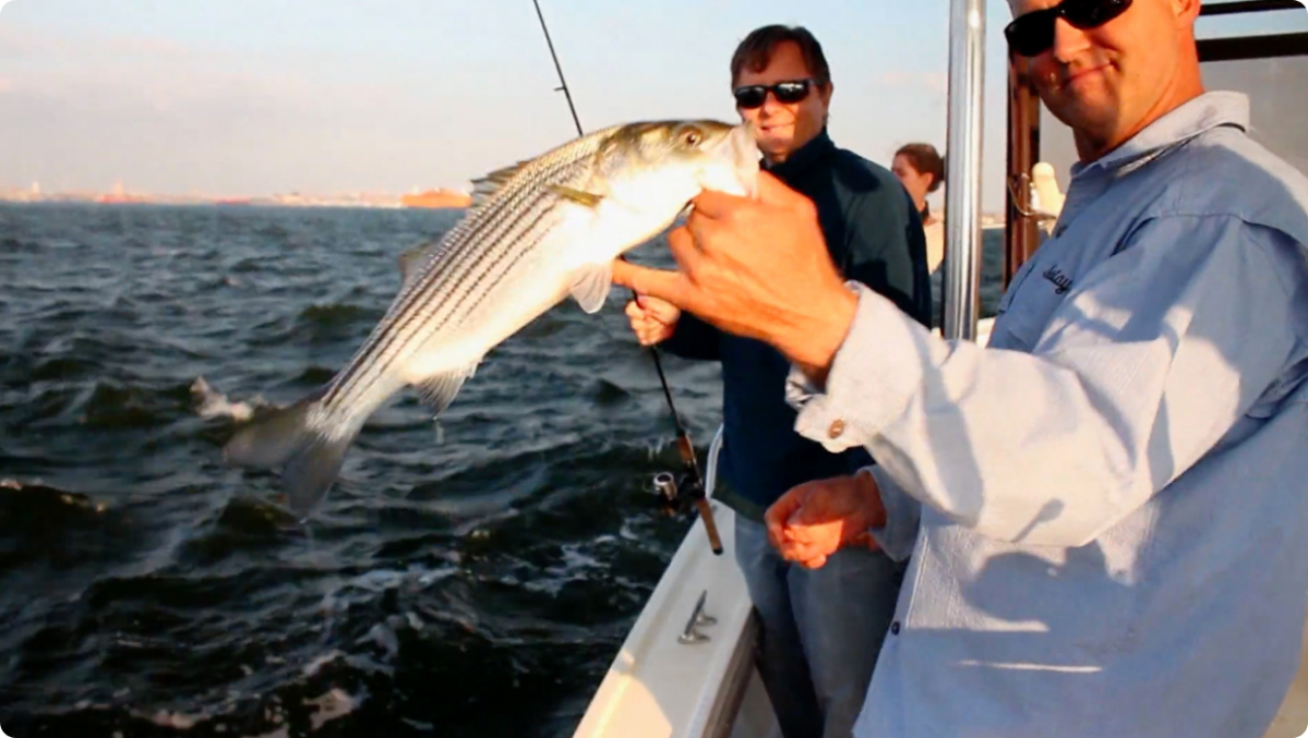 Two men on a boat holding a fish with ocean in the background.