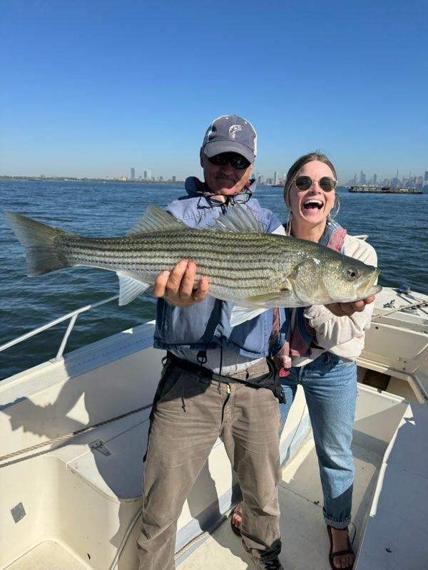 Two people on a boat holding a large fish, smiling against a blue sky.